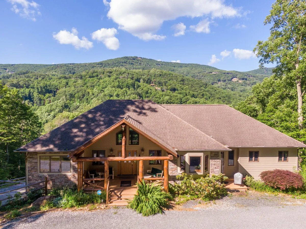 The hero image showcases the cabin's inviting front porch overlooking sweeping mountain vistas, surrounded by lush landscaping. The peaceful setting highlights outdoor dining space—perfect for family gatherings—and the golden glow of sunset dapples the scene, inviting guests to relax and take in the tranquil beauty of Banner Elk.