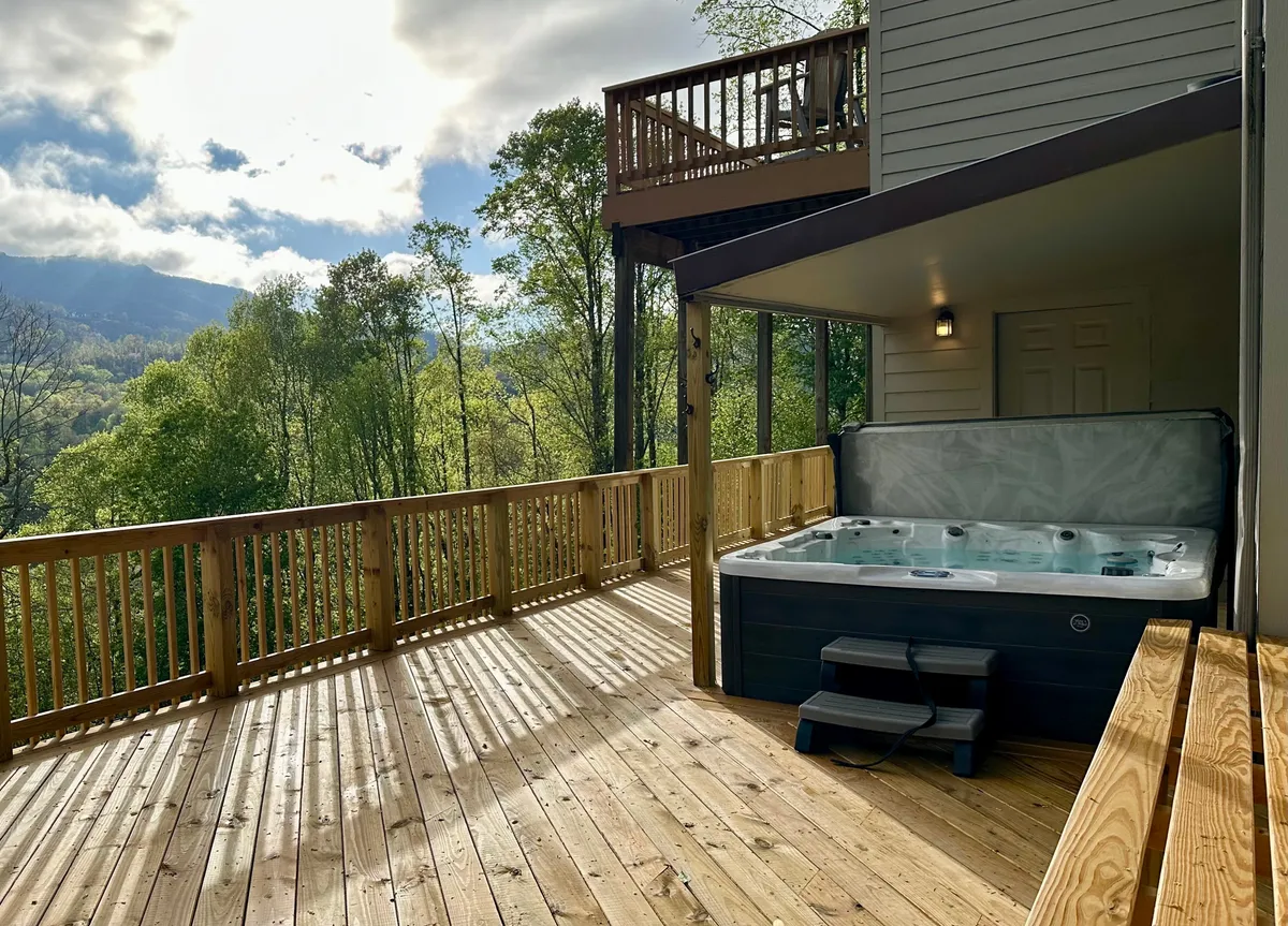 A tranquil mountain-view hot tub sits on a spacious wooden deck, with panoramic vistas stretching into the distance. The deck is inviting for morning coffee, evening relaxation, or hosting outdoor gatherings, embodying both luxury and a connection to nature.