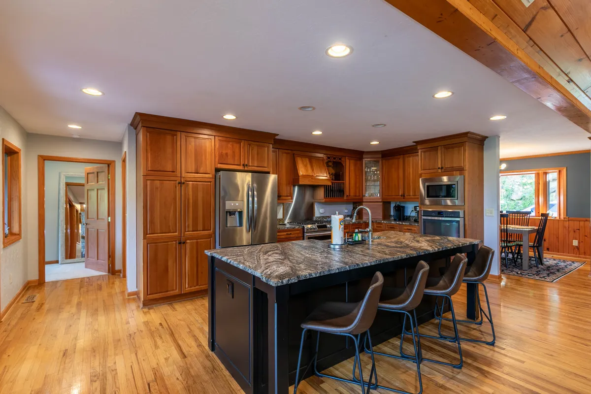 A gourmet kitchen featuring an oversized island with granite countertops, custom cabinetry, modern stainless steel appliances, and a view into the adjacent dining area—conveying open-plan flow and space for entertaining.