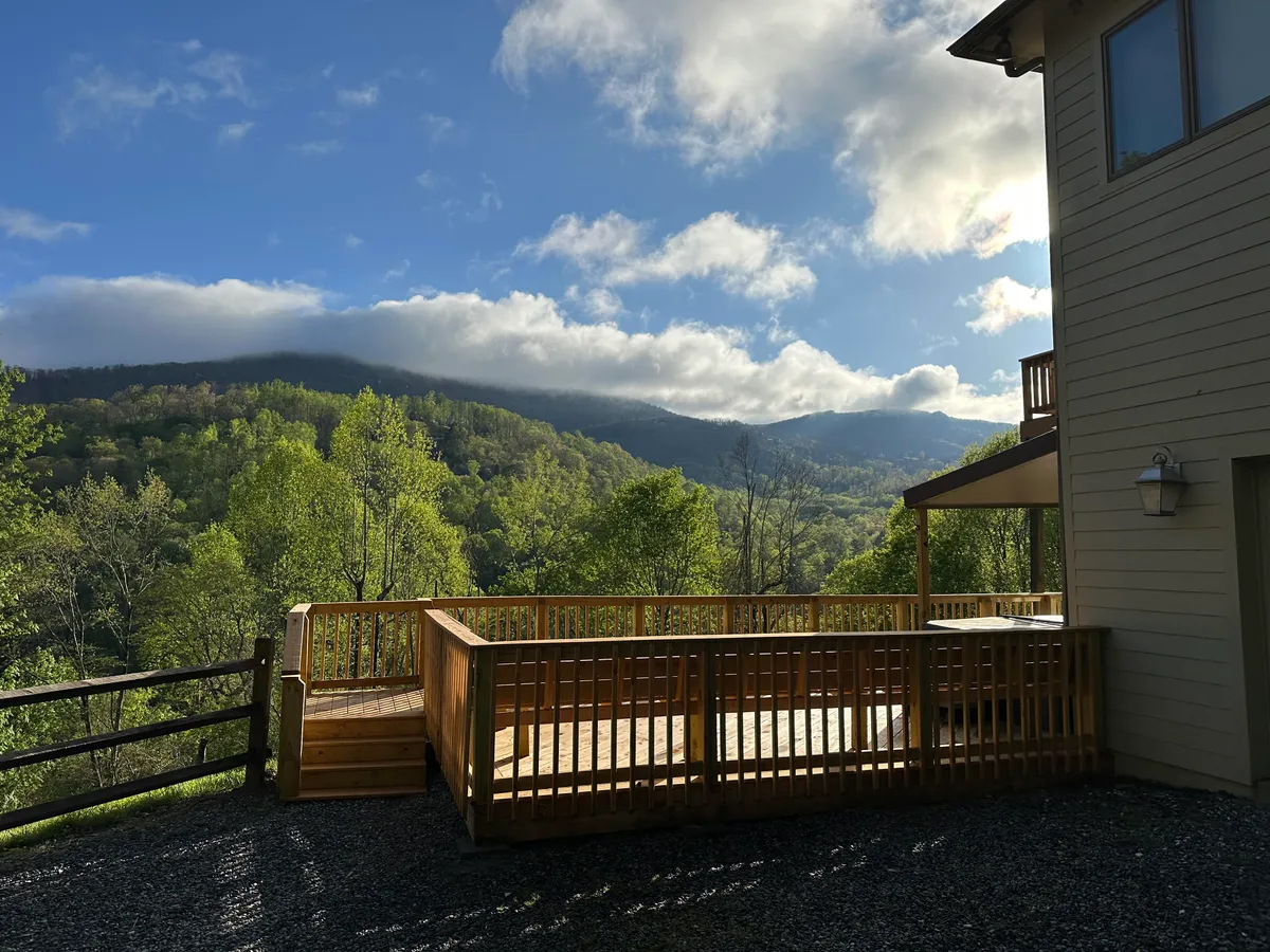 A broad deck overlooking expansive mountain views and vibrant greenery. The deck is outfitted for relaxation, with comfortable seating designed for enjoying morning coffee, sunsets, or simply soaking in the panorama. The surrounding scenery provides a quintessential mountain retreat atmosphere.