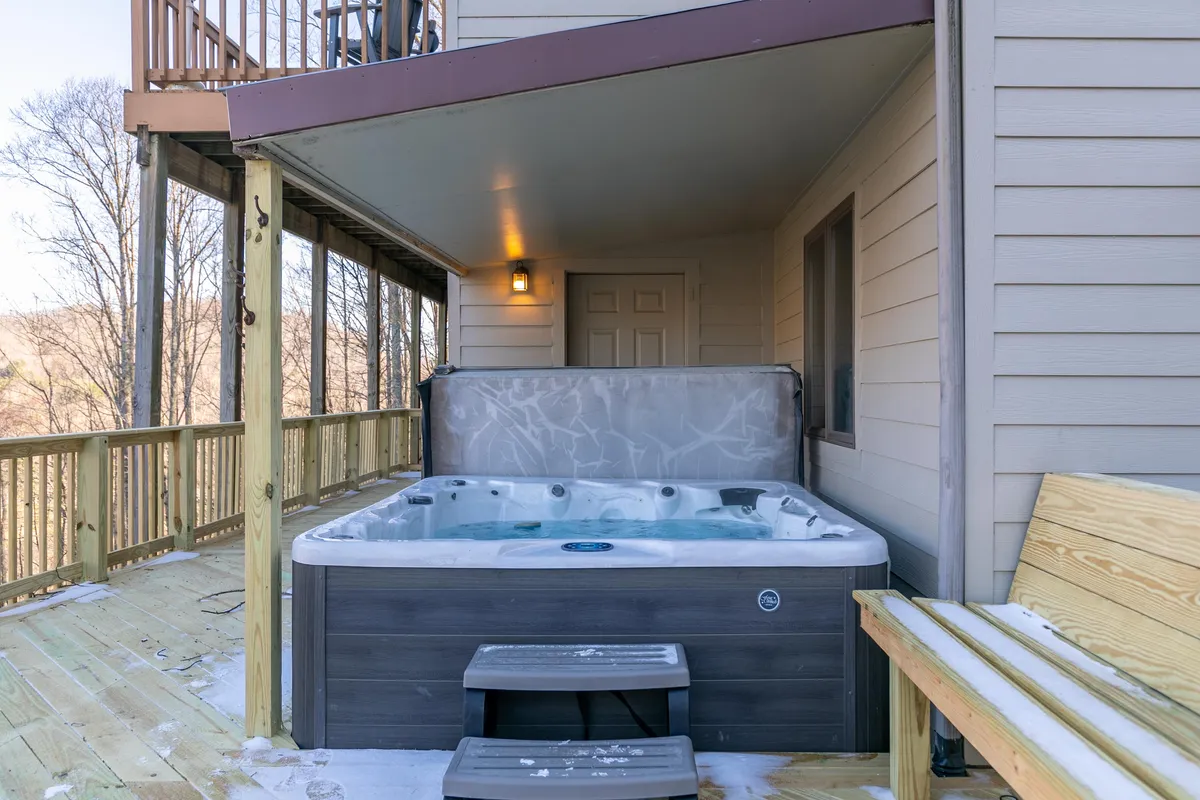 The inviting hot tub sits on a wooden deck with a bench nearby, surrounded by mountain scenery. The space is ideal for soaking in the view after a day of adventure, whether under the sun or stars.