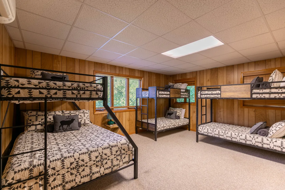 A playful and inviting bunk room with multiple bunk beds outfitted in textured bedding, ample windows streaming in daylight, and a cheerful atmosphere ideal for kids or teens. The layout encourages socialization and sleepover fun.