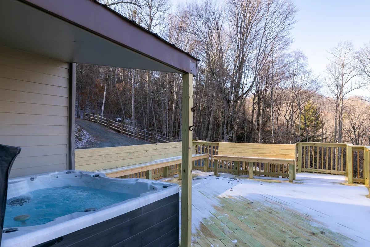 A serene wooden deck with a private hot tub, surrounded by lush trees. The deck offers ample space for group relaxation, and the hot tub is strategically placed to provide sweeping views while enjoying a soak. The natural setting invites guests to unwind in comfort and privacy.
