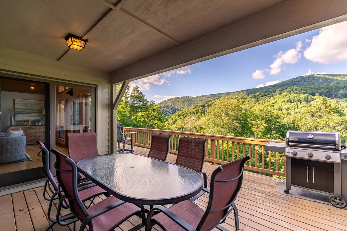 An outdoor deck set with a dining table, grill, and panoramic mountain views, inviting guests to enjoy al fresco meals and sunsets under open skies.